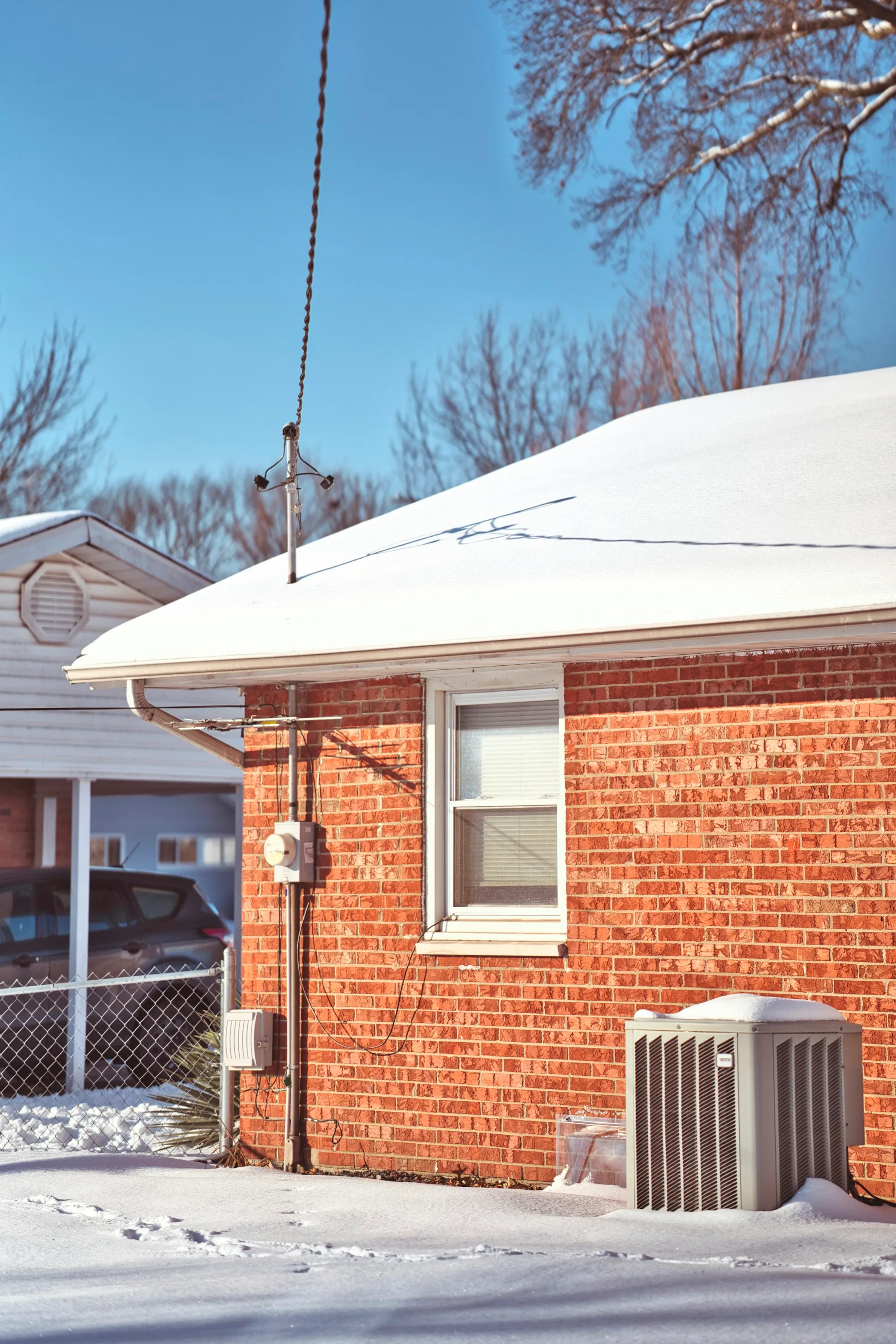 A brick house in the snow with its outdoor heat pump unit